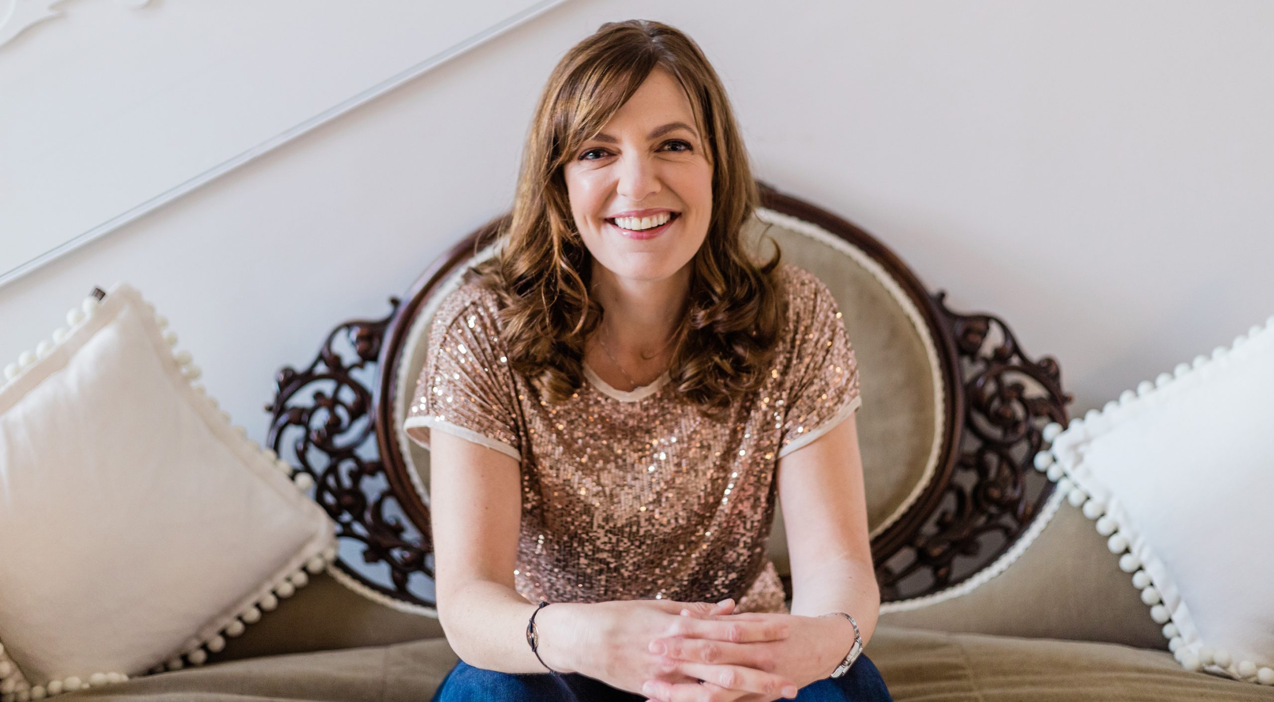 Sinead Doohan at The Happy Me wearing a gold sparkly top, sitting on a chair and smiling