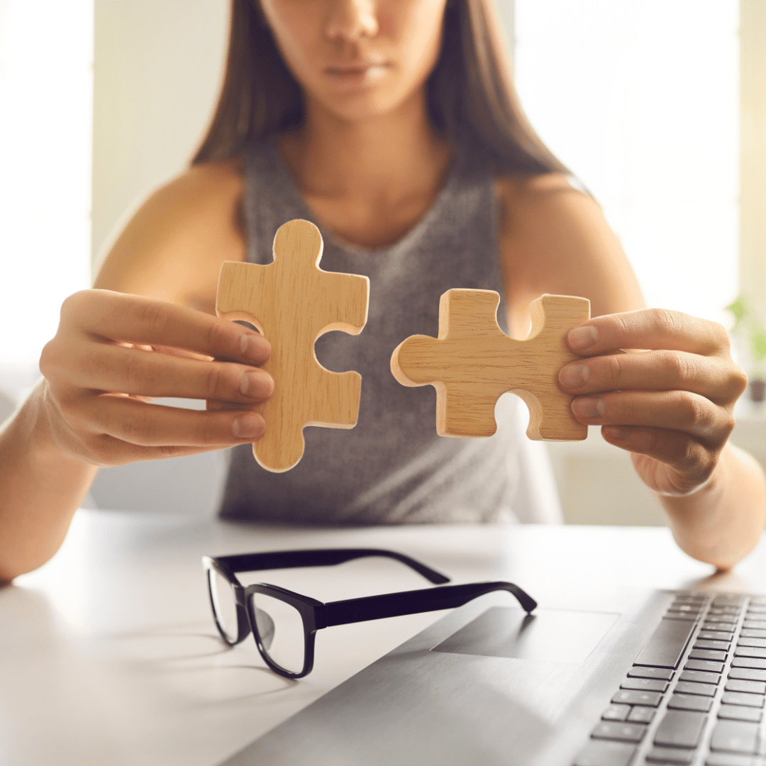 Girl putting two pieces of a wooden jigsaw together. Reading glasses and keyboard sitting on a table