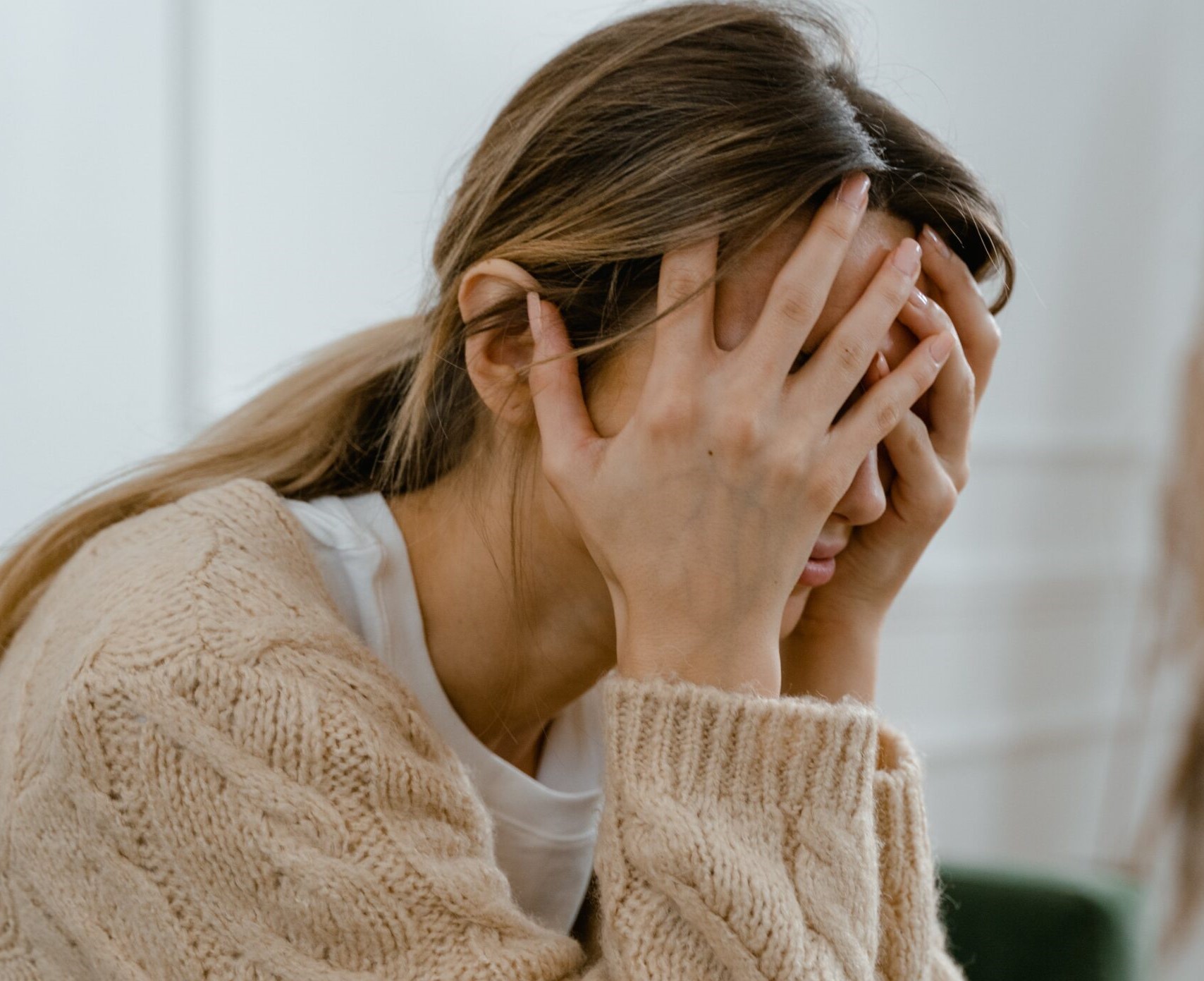 Women wearing a cream knit, sitting looking stressed with head in her hands